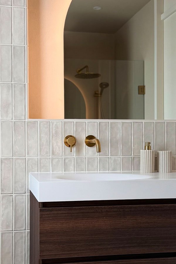 Robinet doré, carrelage blanc et meuble en bois dans la salle de bains de Marloes